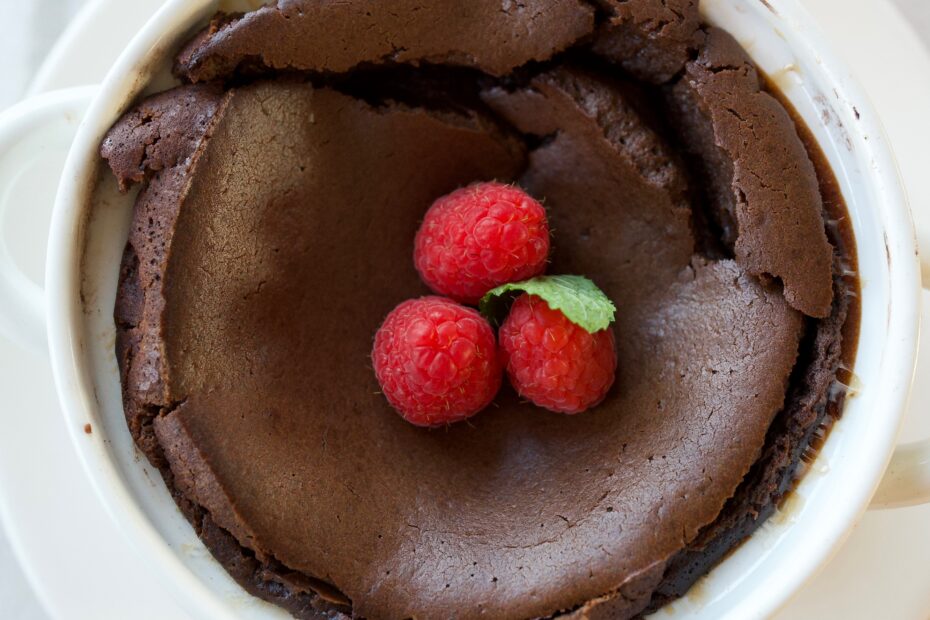 Tall espresso-infused chocolate soufflé in ramekin dusted with powdered sugar, topped with fresh raspberries, mint, and whipped cream-dramatic airy dessert