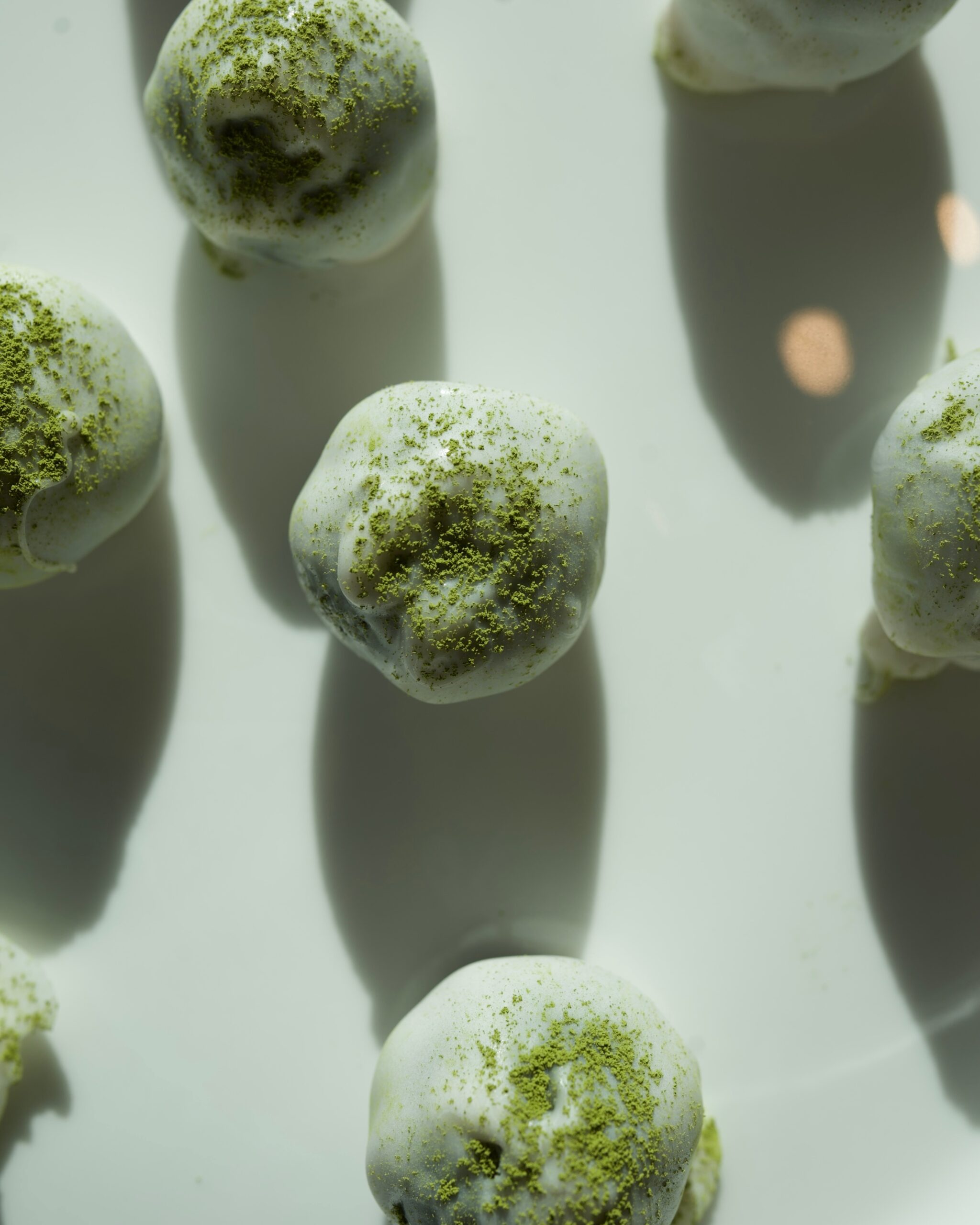 No-bake matcha protein balls dipped in white chocolate and dusted with vibrant green matcha powder – healthy high-protein snack