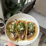Authentic Mexican street-style carne asada tacos topped with cilantro, onion, and salsa on a rustic wooden board
