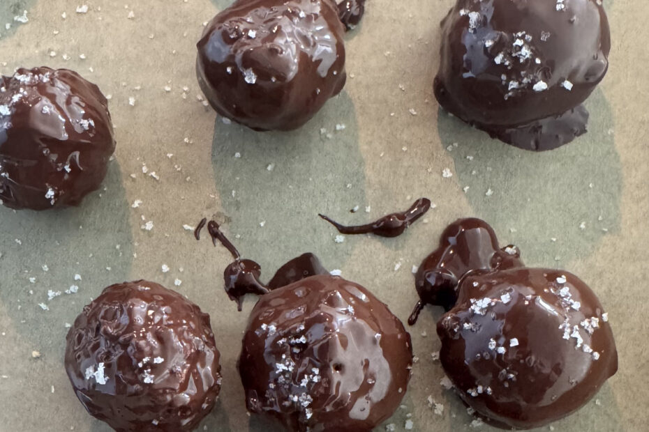 No-bake chocolate coconut protein balls drizzled with dark chocolate and sprinkled with Celtic sea salt on parchment paper