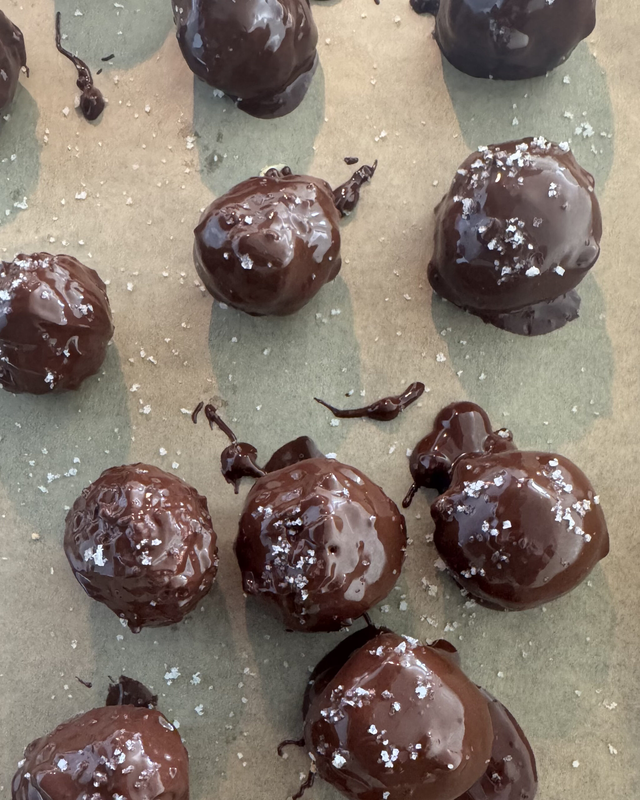 No-bake chocolate coconut protein balls drizzled with dark chocolate and sprinkled with Celtic sea salt on parchment paper
