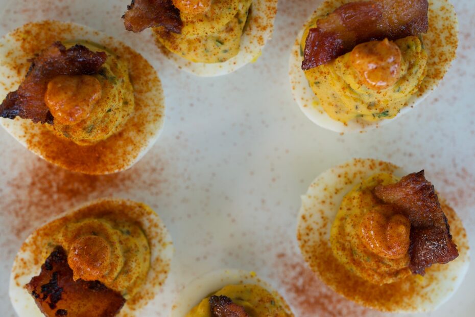 Gourmet bacon deviled eggs topped with smoky paprika mayo, candied bacon pieces, and herbs on a platter