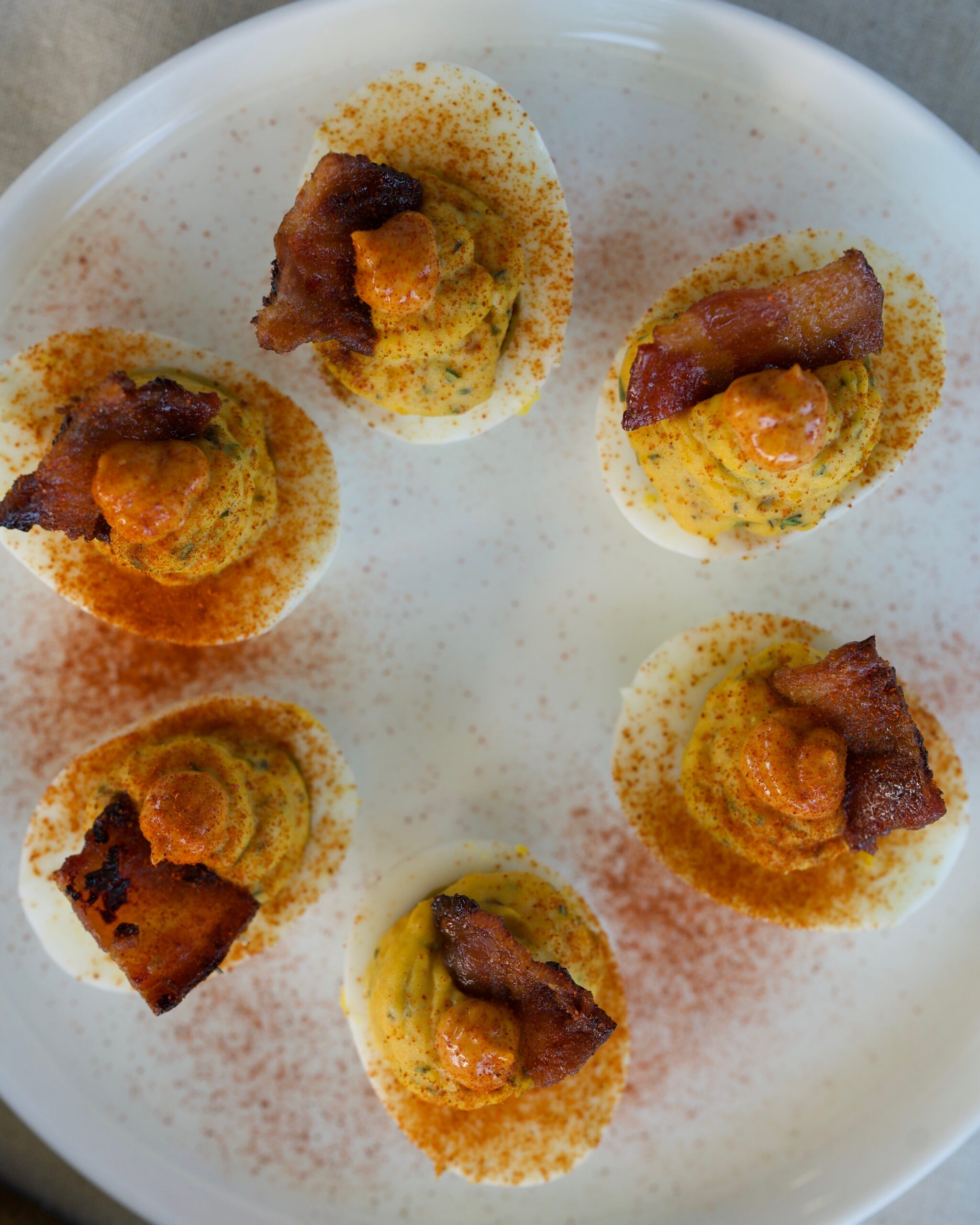 Gourmet bacon deviled eggs topped with smoky paprika mayo, candied bacon pieces, and herbs on a platter