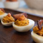 Gourmet bacon deviled eggs topped with smoky paprika mayo, candied bacon pieces, and herbs on a platter