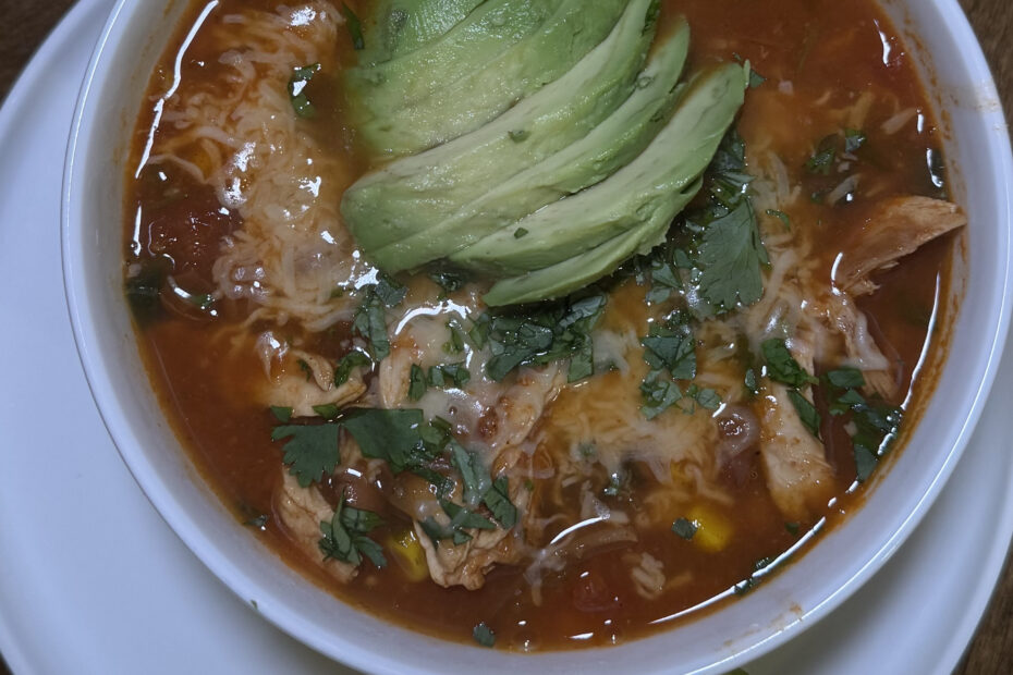 Smoky chicken tortilla soup in bowl topped with sliced avocado, shredded mozzarella, tortilla strips, fresh cilantro, and onion – hearty Tex-Mex comfort food