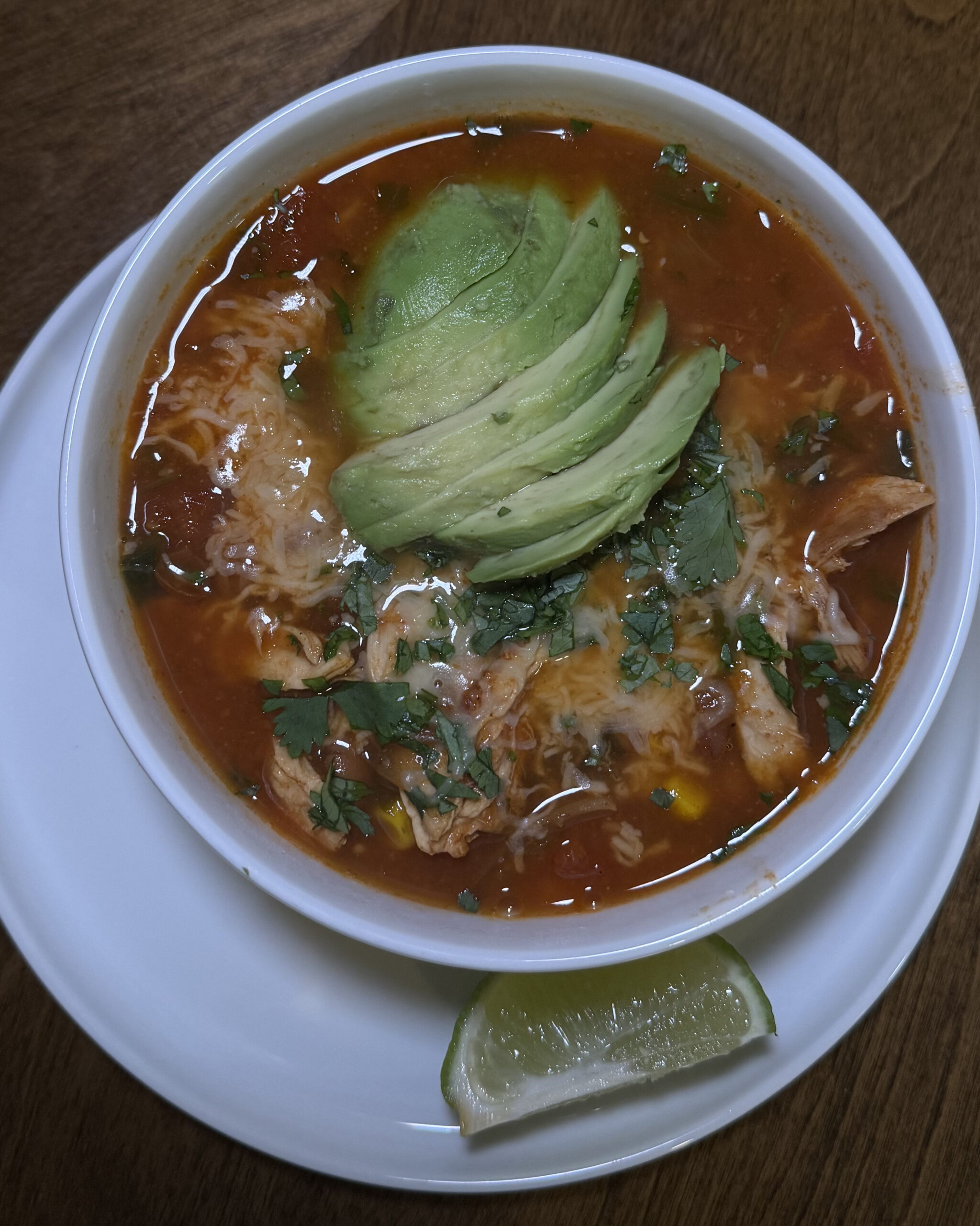 Smoky chicken tortilla soup in bowl topped with sliced avocado, shredded mozzarella, tortilla strips, fresh cilantro, and onion – hearty Tex-Mex comfort food