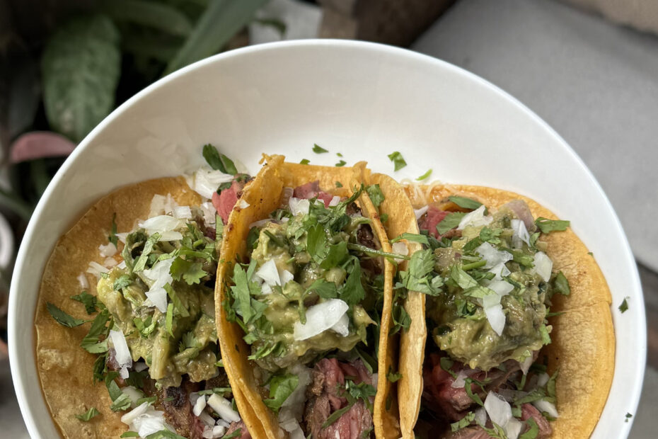 Authentic Mexican street-style carne asada tacos topped with cilantro, onion, and salsa on a rustic wooden board